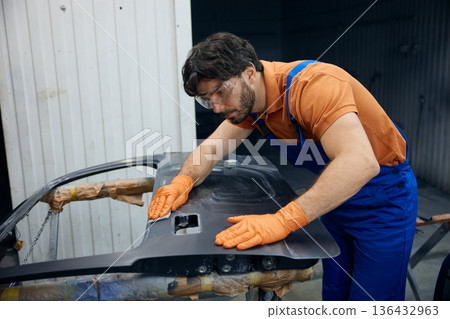 An technician skillfully restoring a car door in a busy garage workshop space An technician skillfully restoring a car door in a busy garage workshop space 136432963