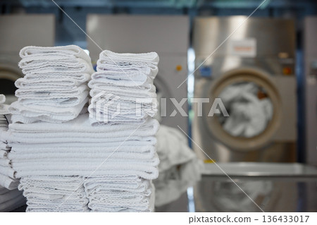 A stack of clean towels is on a table in front of a washing machine 136433017