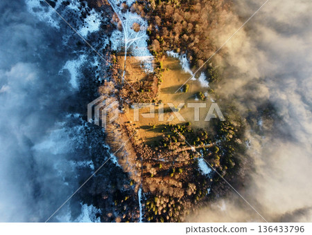 Aerial view of mist-covered landscape where sunlight penetrates through clouds, revealing mix of land and dense forest. Shadows of trees and mist create dramatic interplay of light and dark. Aerial view of mist-covered landscape where sunlight penetrates through clouds, revealing mix of land and dense forest. Shadows of trees and mist create dramatic interplay of light and dark. 136433796