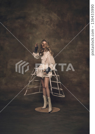 Woman in white dress wearing cage skirt frame standing on platform. 136433990