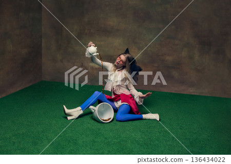 Woman pouring tea into oversized cup in whimsical studio setting. 136434022