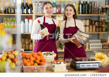 Young saleswomen are holding champagne, wine and sweets in their hands. 136434024