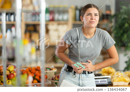 Young woman suffers from abdominal pain, feels pain in her stomach, while visiting grocery supermarket 136434067