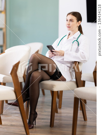 Attentive positive young girl medical student sitting and listening lecture, taking photo or QR with mobil in lecture hall Attentive positive young girl medical student sitting and listening lecture, taking photo or QR with mobil in lecture hall 136434118