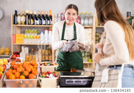 Female seller offers to buy candies to woman in interior of grocery supermarket 136434185