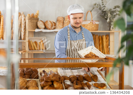 Baker places hot croissants on display in shop 136434208