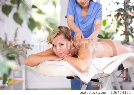 Woman relaxing while professional masseuse doing back massage 136434333