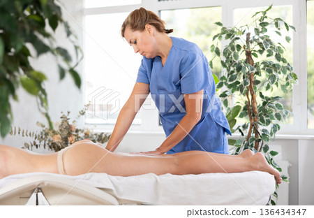 Experienced masseuse doing glutes and hamstrings massage to young woman 136434347