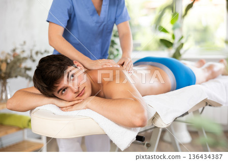 Cropped circumcised young woman performs back shoulder massage to male client. Cropped circumcised young woman performs back shoulder massage to male client. 136434387