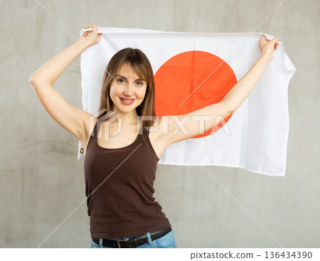 Happy young woman holding flag of Japan against unicoloured background 136434390