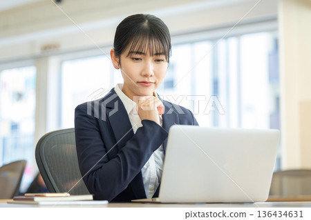 A woman in a suit looking at a laptop computer and worrying 136434631