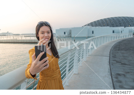 Fashionable Young Asian Woman Taking Selfie Outside museum area in Abu Dhabi United Arab Emirates Fashionable Young Asian Woman Taking Selfie Outside museum area in Abu Dhabi United Arab Emirates 136434877