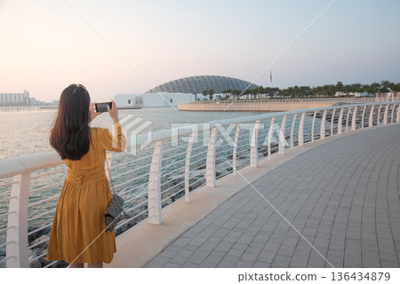 Rear View of Fashionable Young Woman Taking Photo Outside Louvre Abu Dhabi at Sunset Rear View of Fashionable Young Woman Taking Photo Outside Louvre Abu Dhabi at Sunset 136434879