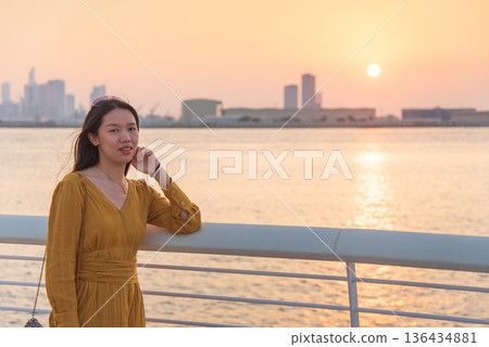 Portrait of Fashionable Asian Woman in Yellow Dress at Sunset with Abu Dhabi Skyline 136434881