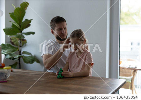 Father and daughter play with a puzzle cube at home, sitting at a wooden table and enjoying mindful time together Father and daughter play with a puzzle cube at home, sitting at a wooden table and enjoying mindful time together 136435054