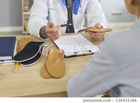 Doctor orthopedist and patient discuss orthopedic insole during consultation Doctor orthopedist and patient discuss orthopedic insole during consultation 136435166