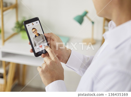 Person using smartphone dating app to like a profile with heart icon closeup 136435169