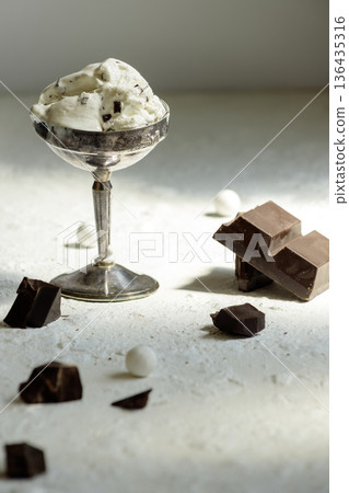 Artistic still life with ice cream in silver ware and dark chocolate pieces.  136435316
