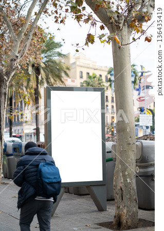 Outdoor blank billboard advertising mockup on an urban street with a person walking by, offering copy space for promoting products, services, or events in a city environment 136435419