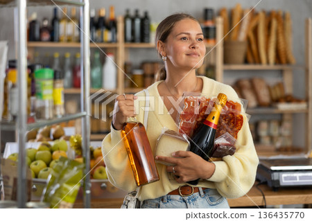 Girl customer stands in sales area of store, clutches bunch of groceries to chest 136435770