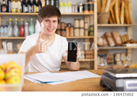 Man with a phone and documents behind the counter in a supermarket 136435802