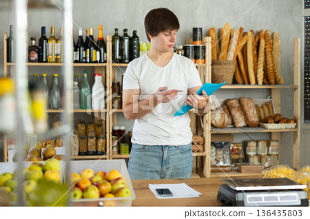 Man seller manager in shop make calculations, work with paper documents and count using phone 136435803