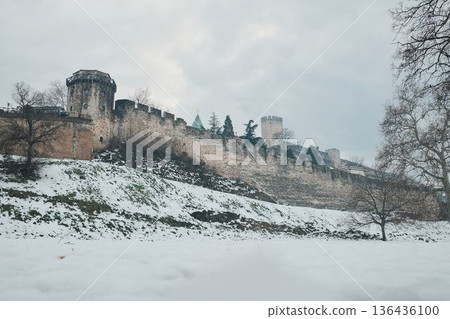 Snow covered park with leafless trees below ancient fortress walls, creating a quiet winter atmosphere and balanced urban landscape 136436100