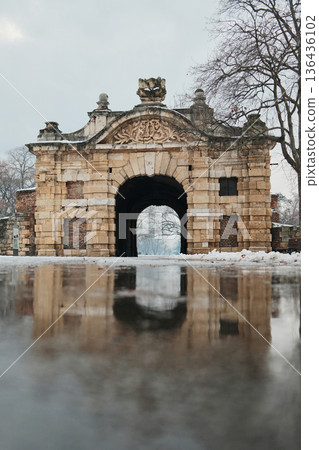 Historic stone fortress gate in winter with snow and wet pavement, showcasing medieval architecture, symmetry, and entrance to an old defensive complex 136436102