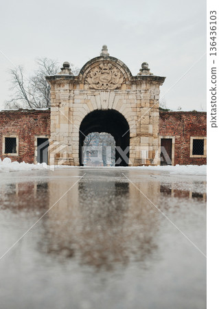 Historic stone fortress gate in winter with snow and wet pavement, showcasing medieval architecture, symmetry, and entrance to an old defensive complex 136436103