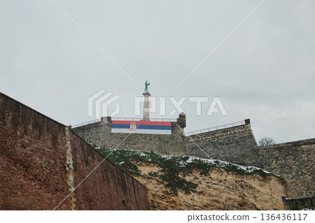 Victor Monument standing on a column above Kalemegdan Fortress with snowy slopes and stone walls in Belgrade Serbia. Symbol of victory national memory and historic landmark concept 136436117