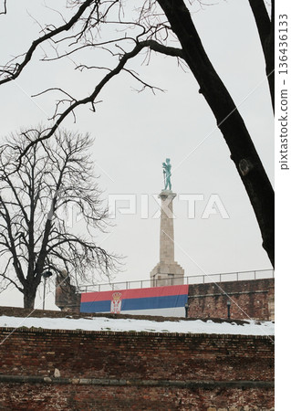 Victory Monument framed by bare winter trees and Serbian flag on Kalemegdan walls, combining nature, history and national identity in Belgrade Victory Monument framed by bare winter trees and Serbian flag on Kalemegdan walls, combining nature, history and national identity in Belgrade 136436133