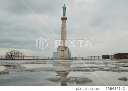 Victory Monument in Kalemegdan Fortress reflected in wet stone surface after snow, creating dramatic symmetry and minimalist winter city landmark composition Victory Monument in Kalemegdan Fortress reflected in wet stone surface after snow, creating dramatic symmetry and minimalist winter city landmark composition 136436142