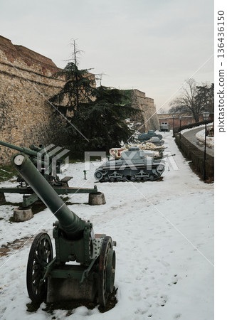 Military exhibition with tanks and artillery displayed along fortress wall in Kalemegdan, Belgrade, surrounded by snow and historic stone fortifications 136436150