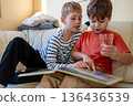 Two boys sitting on a sofa reading a book together at home 136436539