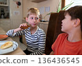 Two elementary age boys talking while having a snack at home 136436545