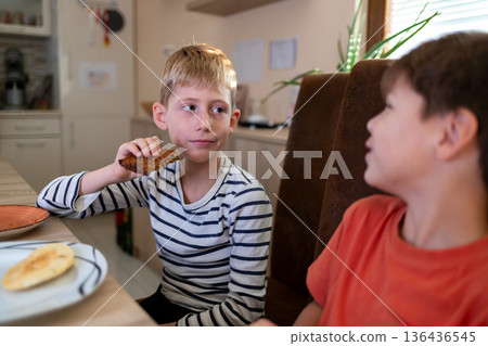 Two elementary age boys talking while having a snack at home 136436545