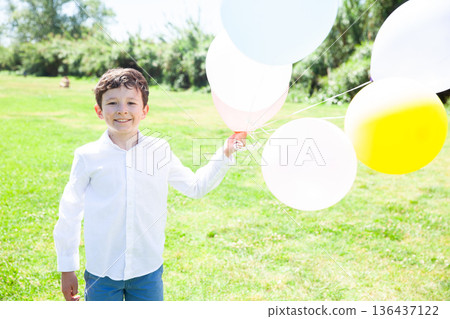 Joyful tween boy playing with balloons in green meadow Joyful tween boy playing with balloons in green meadow 136437122