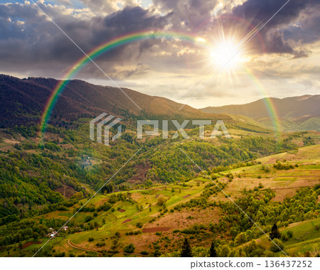 rural mountain landscape during spring at sunset. wonderful countryside scenery on a cold weather in evening light. cloudy sky above rolling hills in may. timeless nostalgia book cover with rainbow 136437252