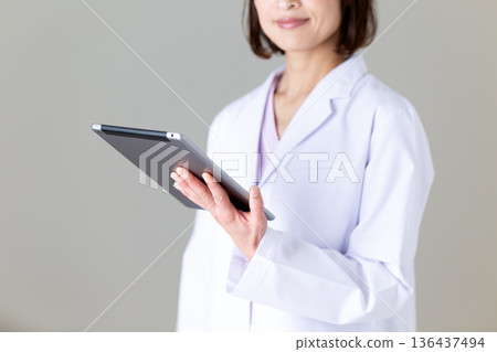 A middle-aged female nurse in a white coat holding a tablet A middle-aged female nurse in a white coat holding a tablet 136437494