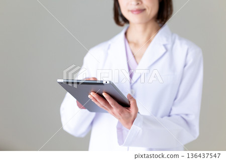 A middle-aged female nurse in a white coat holding a tablet A middle-aged female nurse in a white coat holding a tablet 136437547