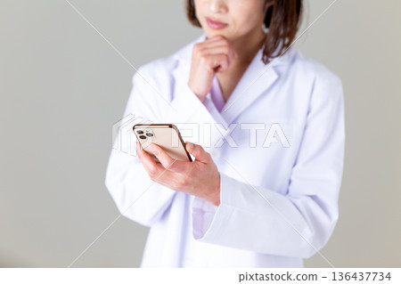 一位身穿白大褂的中年女護士看著她的智慧型手機,憂心忡忡。 一位身穿白大褂的中年女護士看著她的智慧型手機,憂心忡忡。 136437734