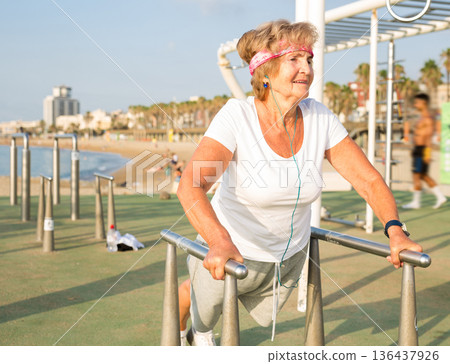 Mature lady exercising on dip station outdoors Mature lady exercising on dip station outdoors 136437926
