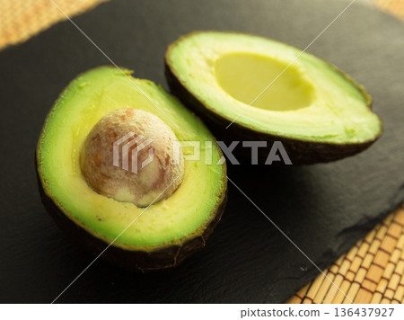 ripe halved avocado with bone on black stone board ripe halved avocado with bone on black stone board 136437927