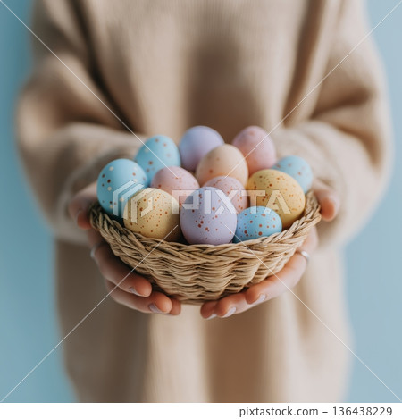 Person holding woven basket with pastel Easter eggs. Easter background. Person holding a small basket filled with colorful speckled Easter eggs in hands 136438229