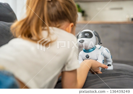 Child playing and interacting with robotic dog on sofa at home. Human robot interaction and digital companionship in modern childhood. Child playing and interacting with robotic dog on sofa at home. Human robot interaction and digital companionship in modern childhood. 136439249