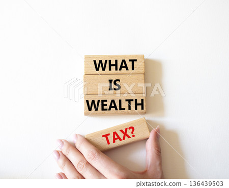 Tax symbol. Concept words What is Wealth Tax on wooden blocks. Beautiful bright white background. Businessman hand. Business and What is Wealth Tax concept. Copy space. Tax symbol. Concept words What is Wealth Tax on wooden blocks. Beautiful bright white background. Businessman hand. Business and What is Wealth Tax concept. Copy space. 136439503