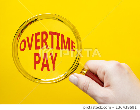 Overtime Pay symbol. Magnifying Glass with words Overtime Pay. Businessman hand. Beautiful yellow background. Business and Overtime Pay concept. Copy space. 136439691