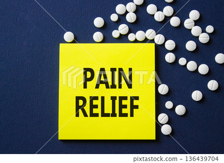 Pain Relief symbol. Concept word Pain Relief on yellow note. Beautiful deep blue background with pills. Medicine and Pain Relief concept. Copy space Pain Relief symbol. Concept word Pain Relief on yellow note. Beautiful deep blue background with pills. Medicine and Pain Relief concept. Copy space 136439704