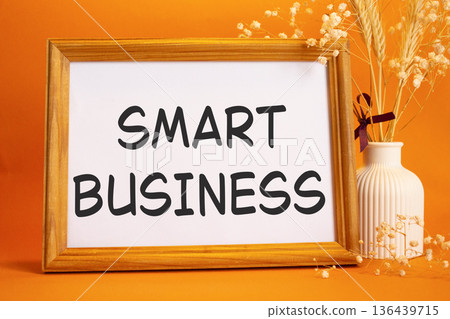 Smart business symbol. Concept words Smart business on beautiful wooden picture frame. Beautiful orange background with flower vase. Business and Smart business concept. Copy space. 136439715