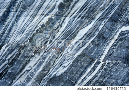 Uneven texture of real blue marble with diagonal white veins and natural cracks. Stone material for surface design, background, or wallpaper. 136439733